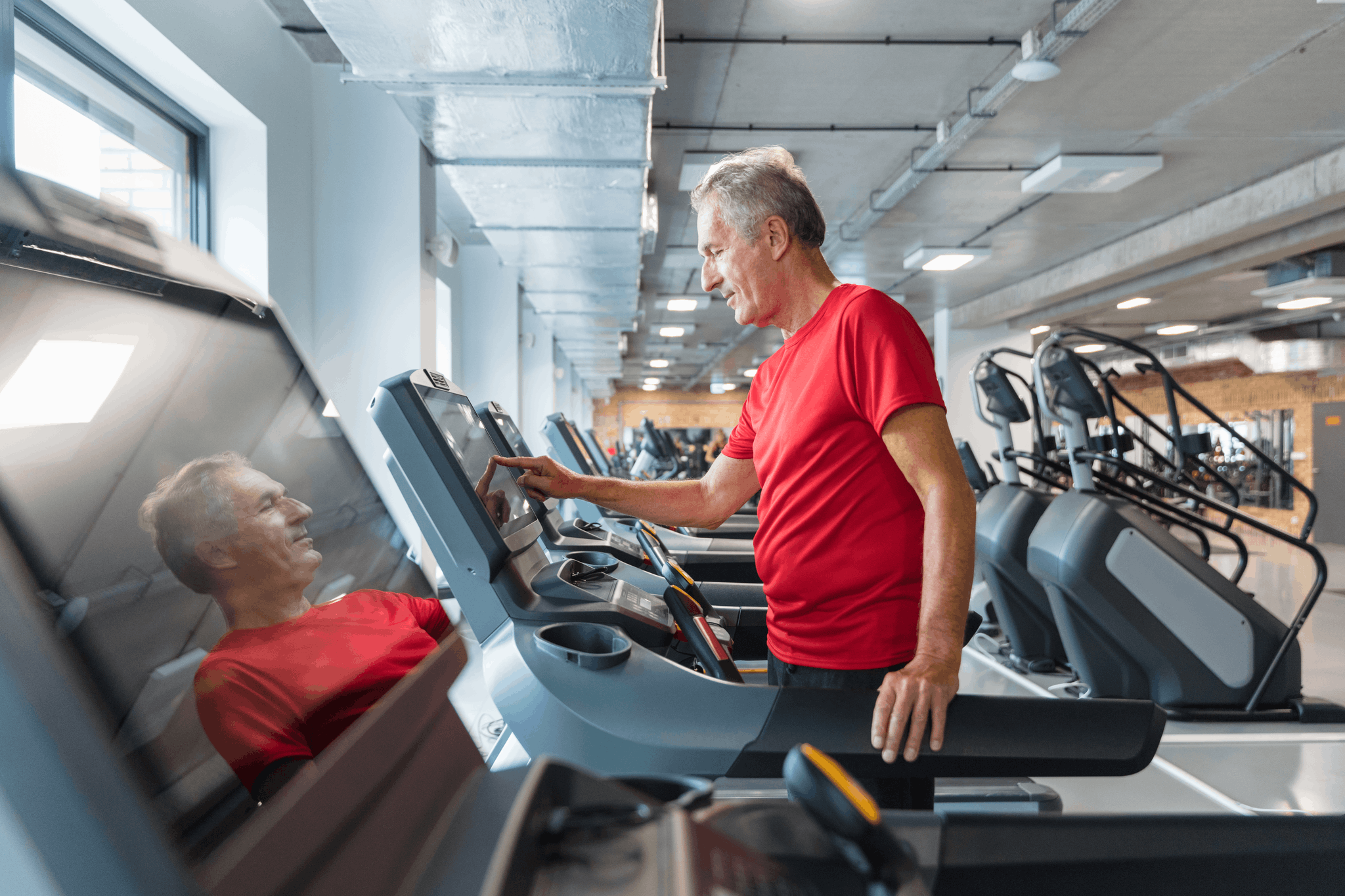 A man in a red t-shirt standing on a treadmill in a fitness center